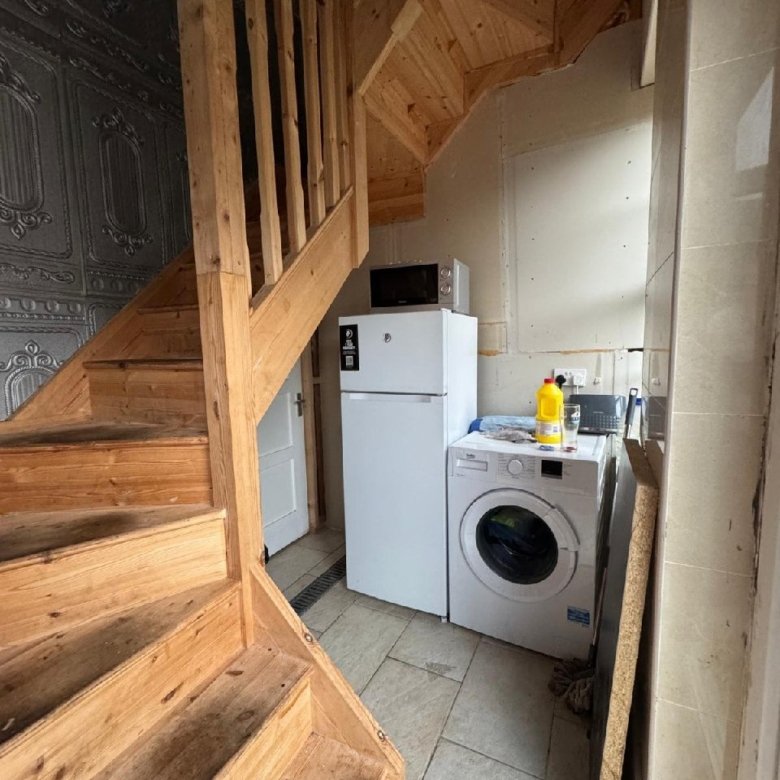 Laundry area under wooden staircase with washer, fridge, and microwave.