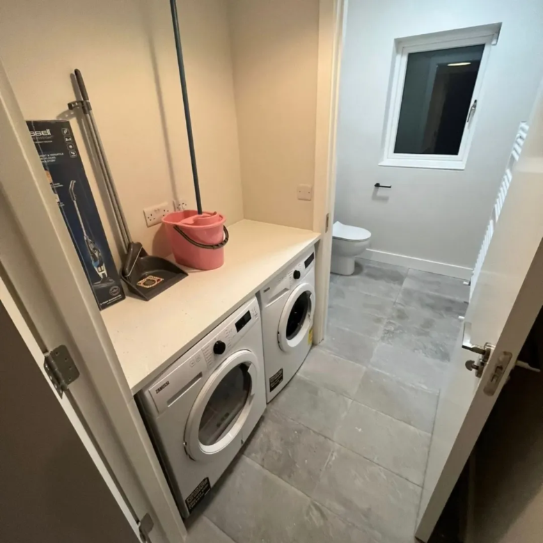 Laundry room with washer, cleaning supplies, and toilet visible through doorway.
