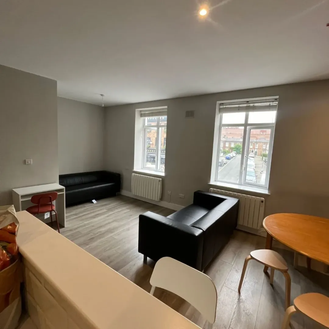 Living room with black sofas, wooden floors, and two windows.