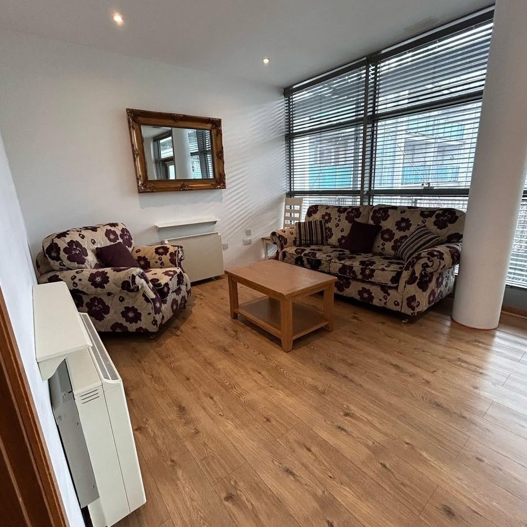 Living room with floral armchair, sofa, wood floor, and large window.