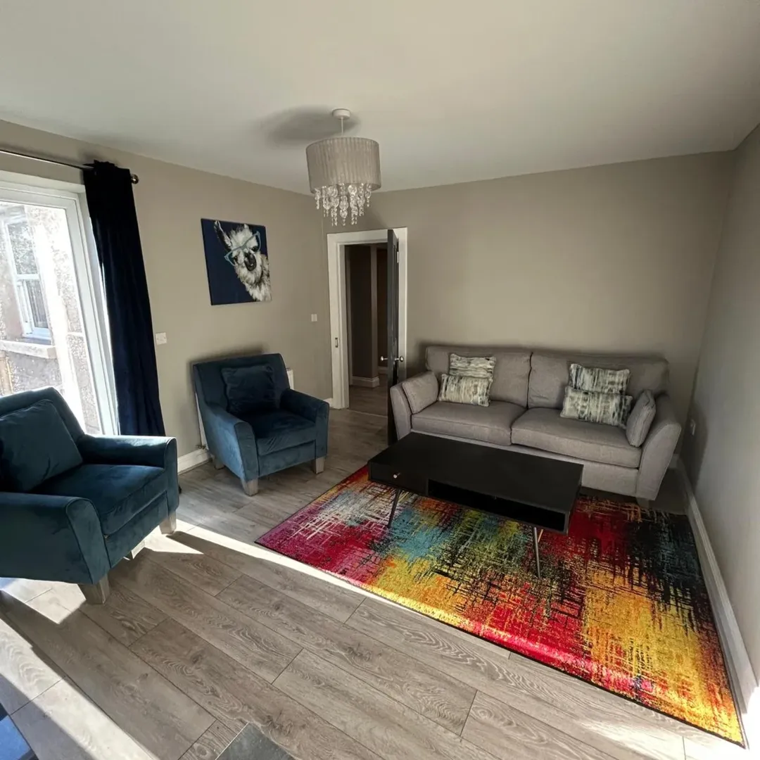 Living room with gray sofa, blue armchairs, and colorful rug.