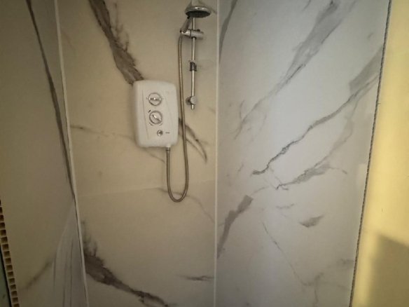 Shower with marble-effect wall panels and electric shower unit.