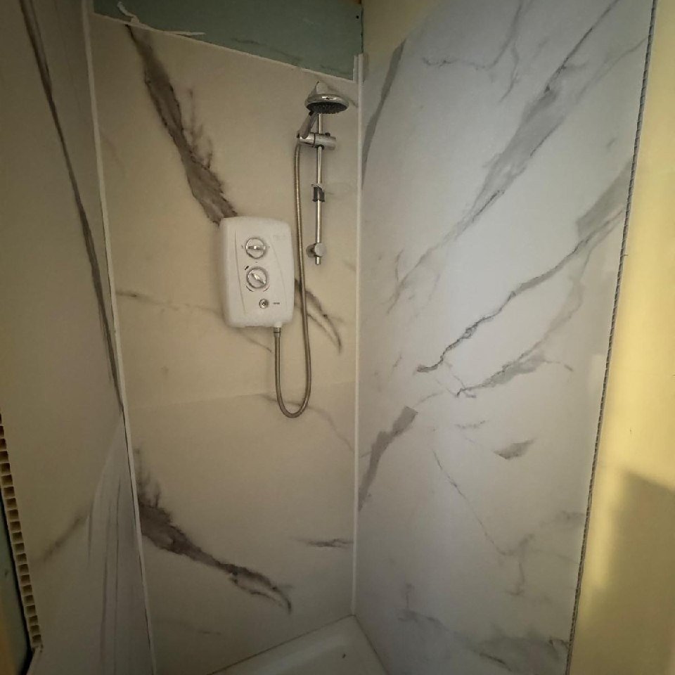 Shower with marble-effect wall panels and electric shower unit.