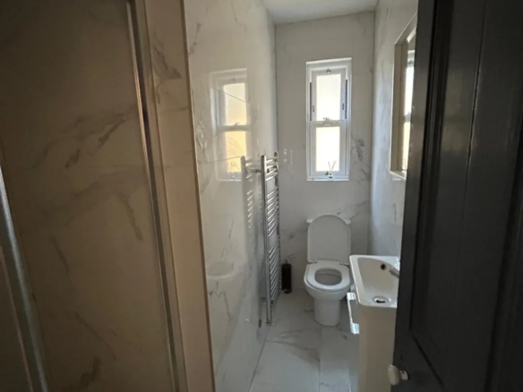 Modern bathroom with shower, toilet, sink, and window.