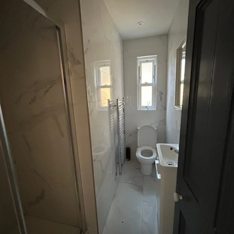 Modern bathroom with shower, toilet, sink, and window.