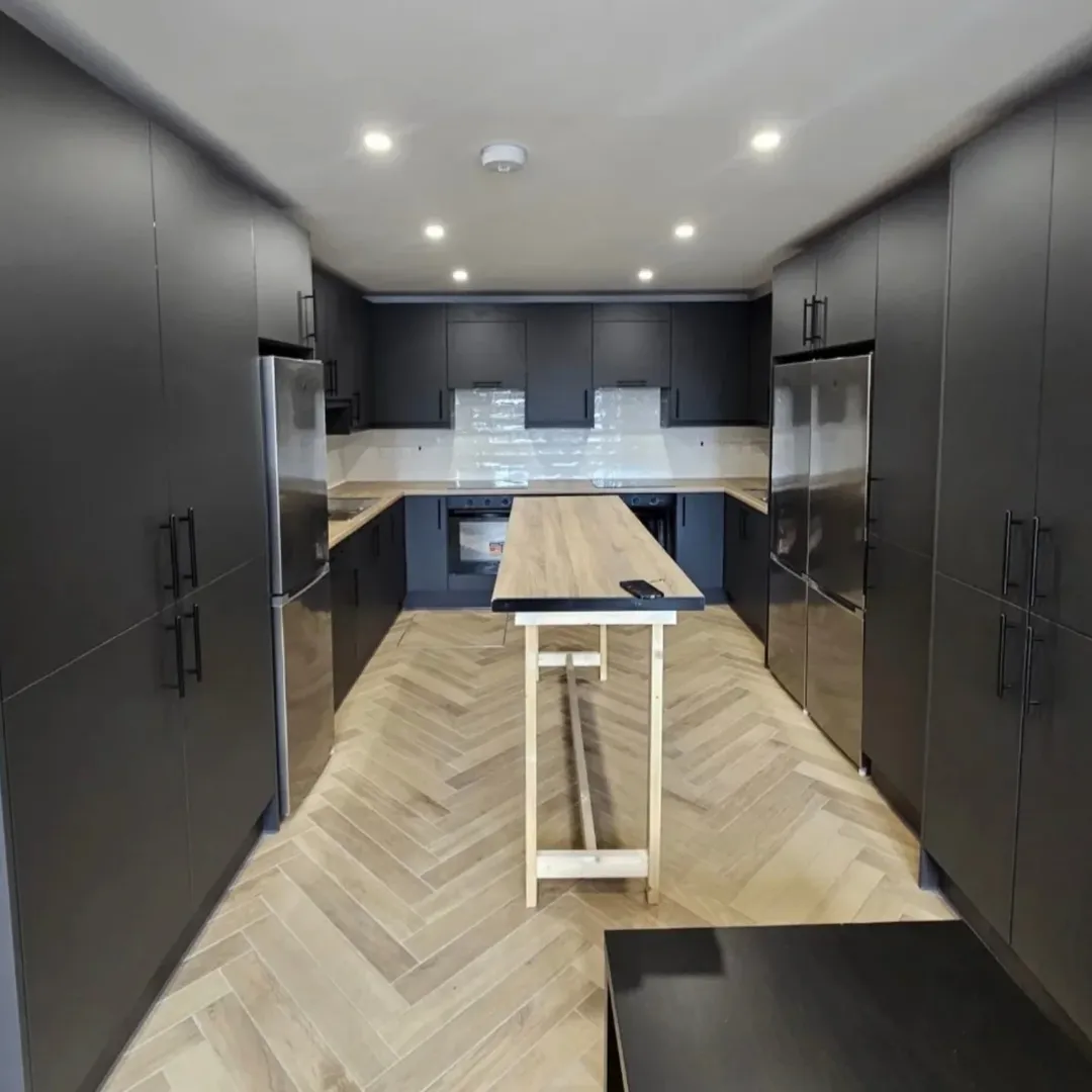 Modern kitchen with dark cabinets, wood island, and herringbone floor.