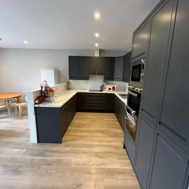 Modern kitchen with gray cabinets, light wood floors, and marble countertops.