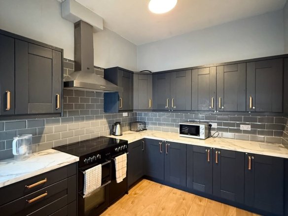 Modern kitchen with dark cabinets, marble countertops, and wood flooring.