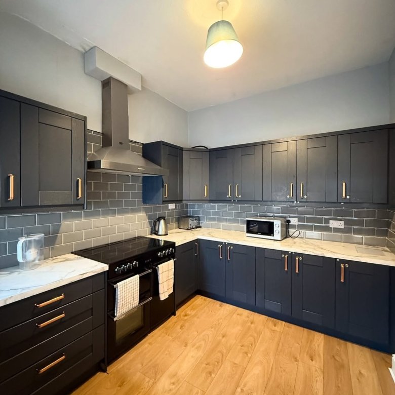 Modern kitchen with dark cabinets, marble countertops, and wood flooring.