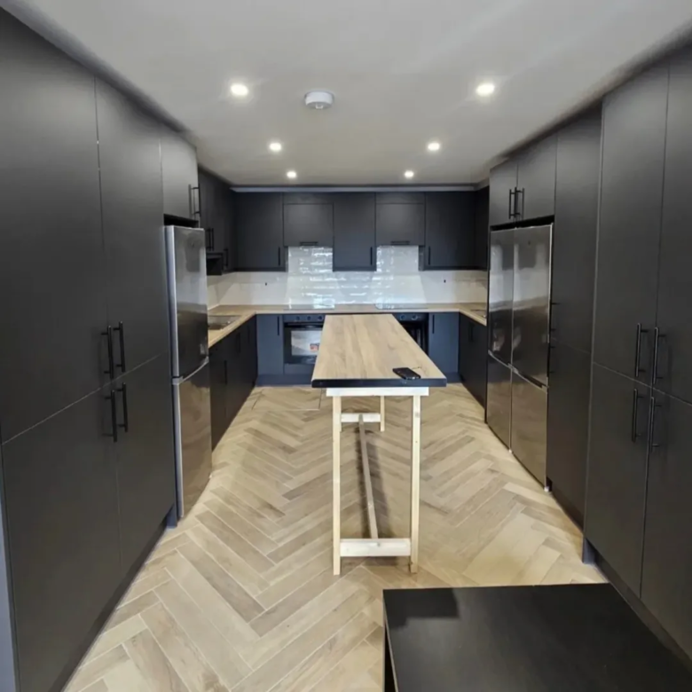 Modern kitchen with dark cabinets, wood island, and herringbone floor.