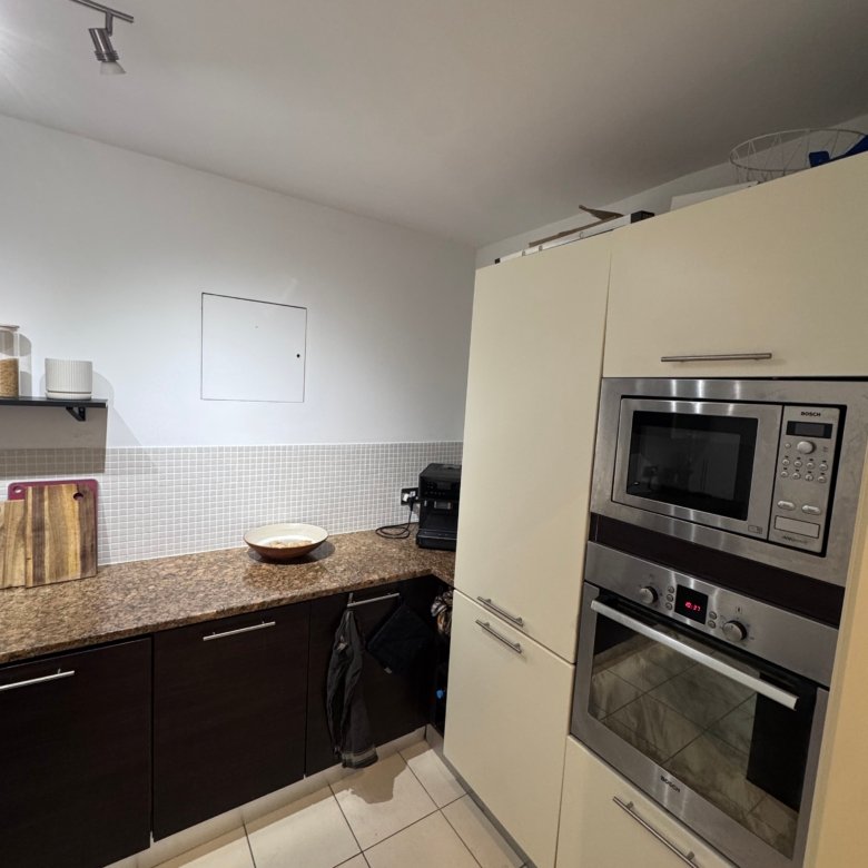 Modern kitchen with built-in stainless steel microwave and oven, cream cabinets, and tiled floor.