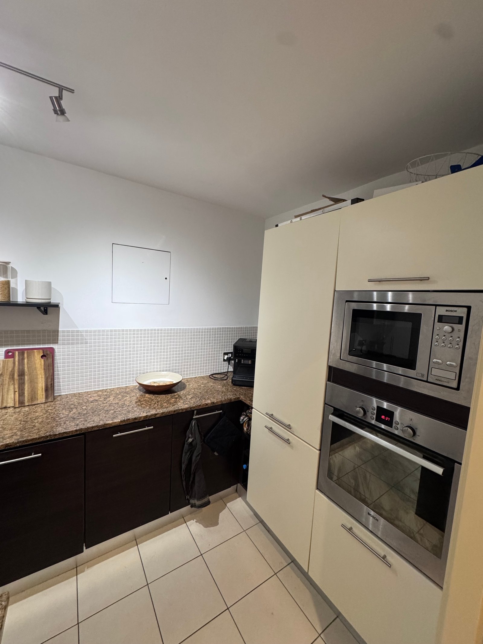 Modern kitchen with built-in stainless steel microwave and oven, cream cabinets, and tiled floor.