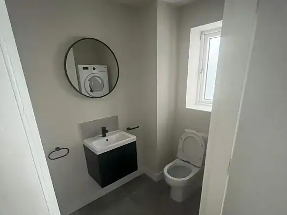 Small modern bathroom with toilet, sink, and round mirror.