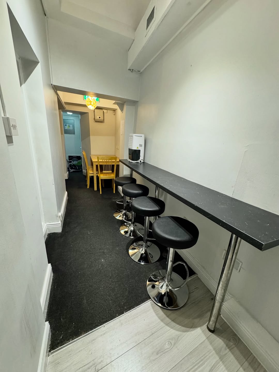 Narrow dining area with bar stools, table, and yellow chairs.