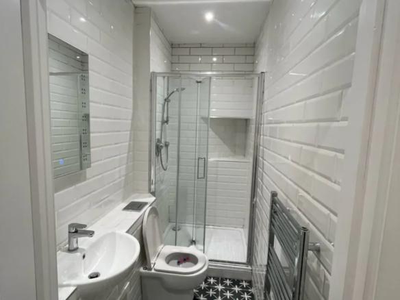 Small bathroom with shower, toilet, sink, black and white tile floor.