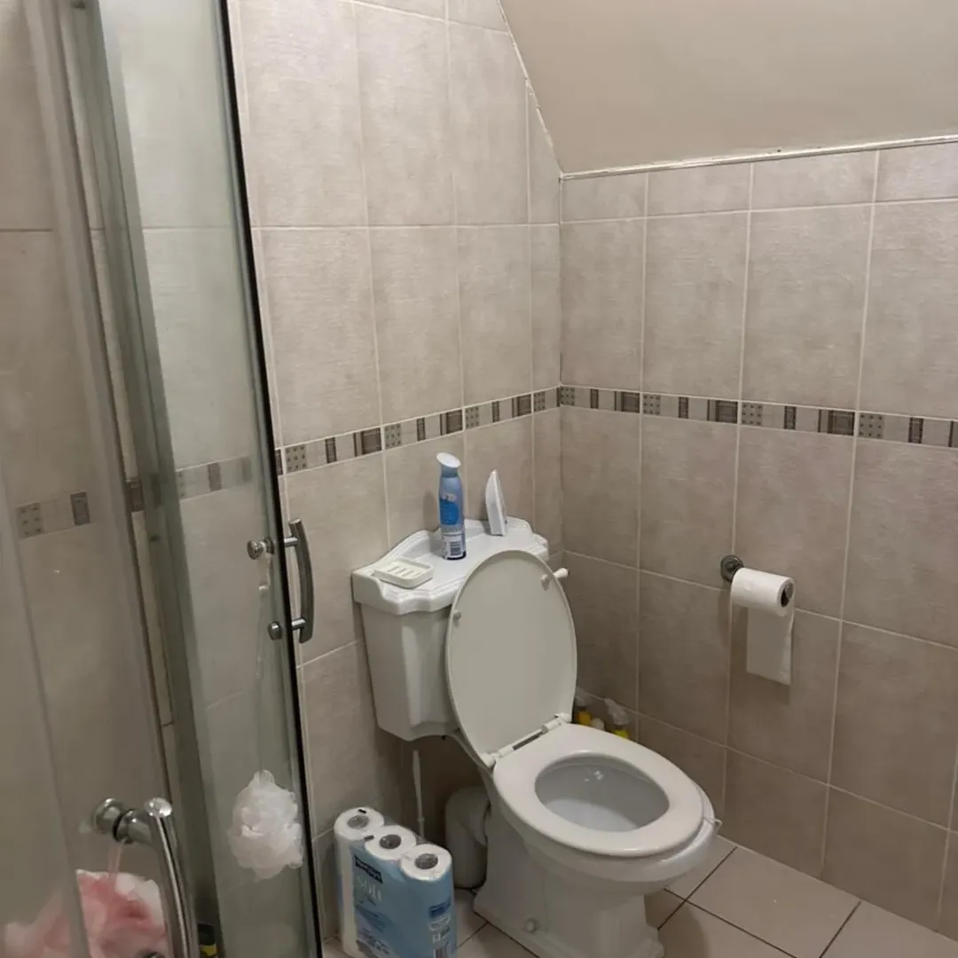 Small bathroom with toilet, shower, and beige tile.