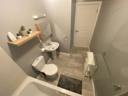 Small bathroom with toilet, sink, shelves, and tiled floor.