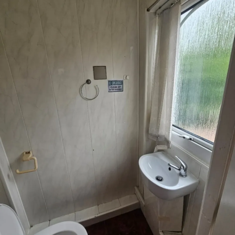 Small bathroom with toilet, sink, window, and "Be considerate, clean up after yourself" sign.