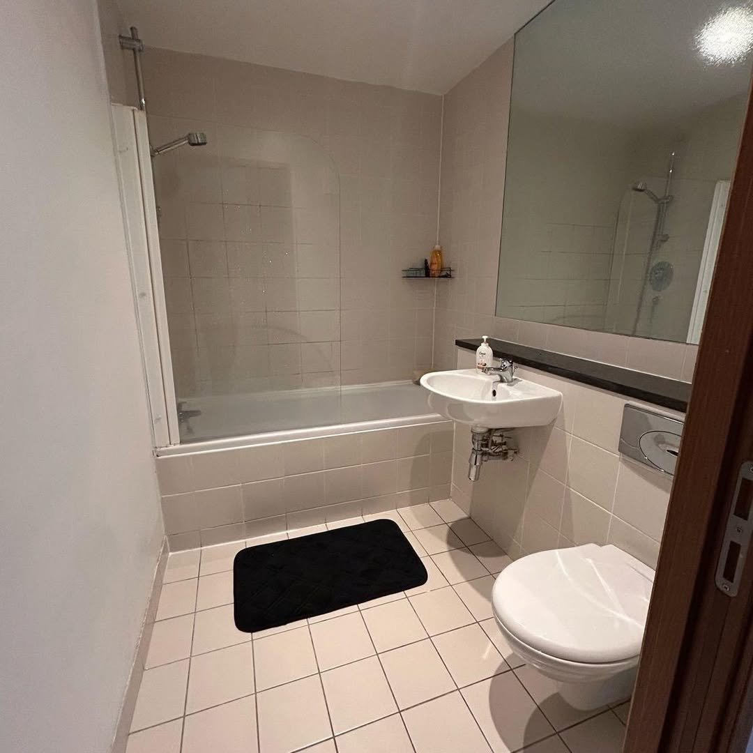 Small bathroom with tub shower, sink, and toilet in neutral tones.