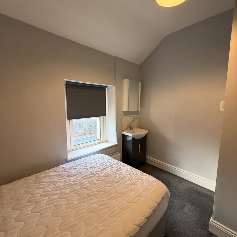 Small bedroom with bed, sink, cabinet, window with blind, gray walls, and dark carpet.