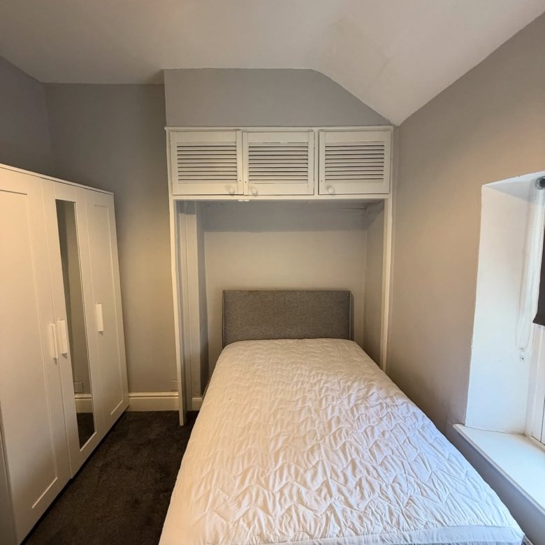 Small bedroom with bed, wardrobe, and overhead storage.