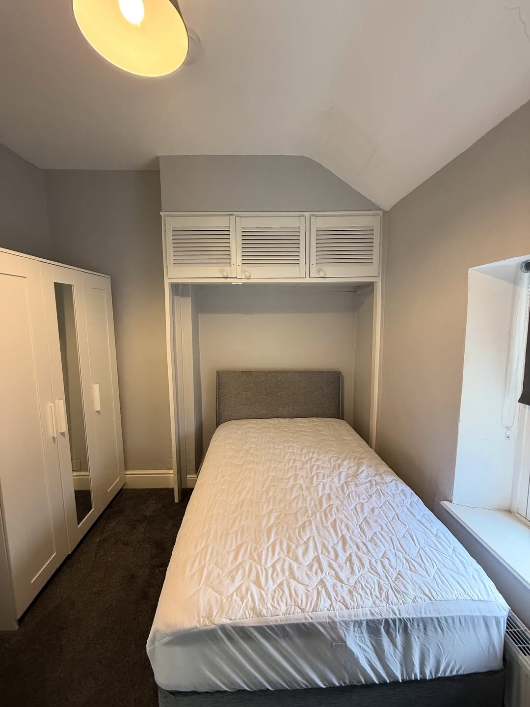 Small bedroom with bed, wardrobe, and overhead storage.