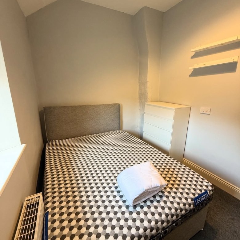 Cozy bedroom with patterned bed, white dresser, and radiator. Simple room interior.