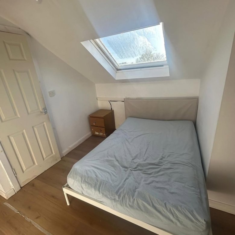 Cozy bedroom with single bed, skylight, and wooden bedside table. Small space, sloped ceiling.