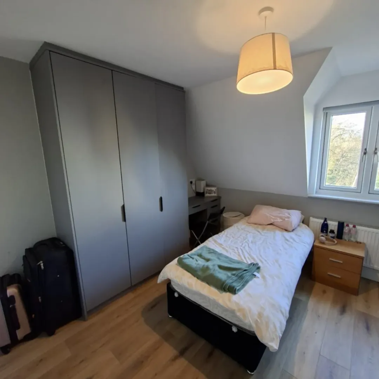 Cozy bedroom with single bed, wardrobe, desk, and natural light from a window.