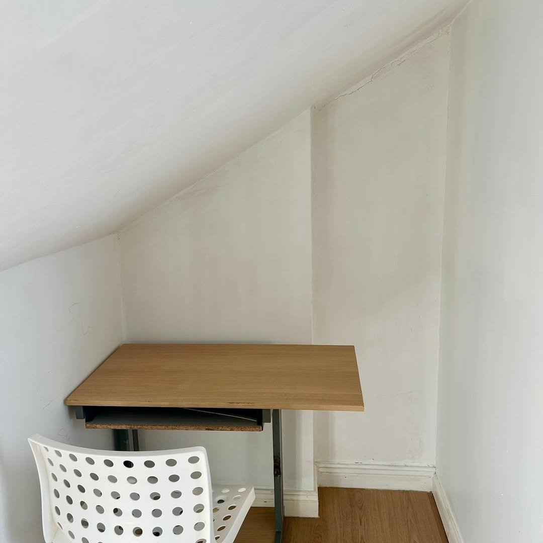 Small desk and chair in a tight corner space with white walls and an angled ceiling.