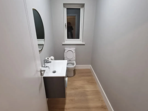 Small gray powder room with toilet, sink, and oval mirror.