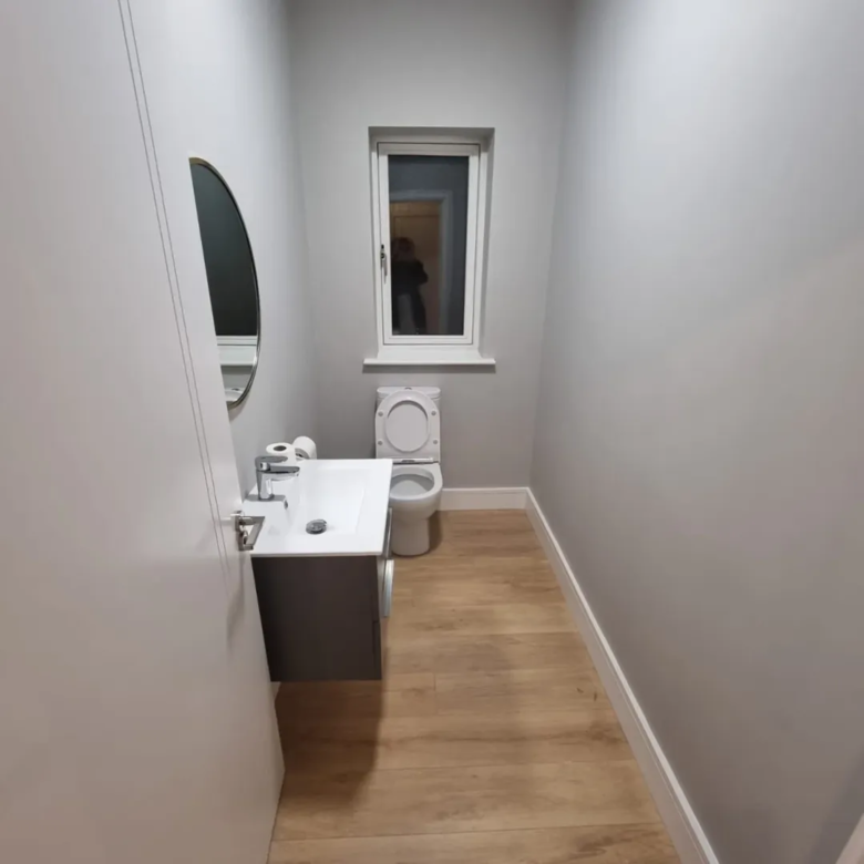 Small gray powder room with toilet, sink, and oval mirror.