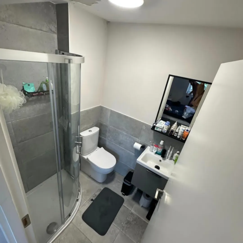 Small bathroom with shower, toilet, and sink. Gray and white color scheme.