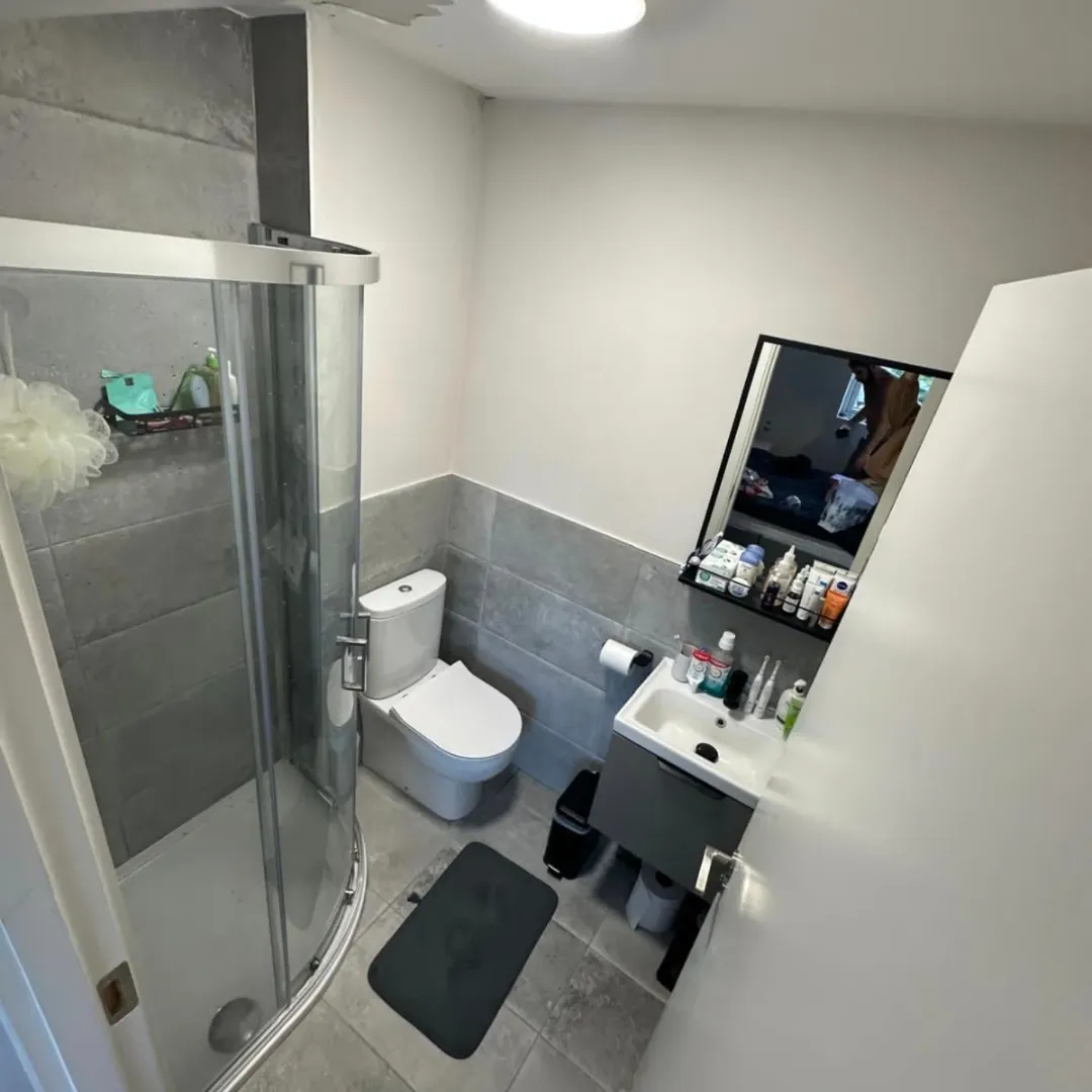 Small bathroom with shower, toilet, and sink. Gray and white color scheme.