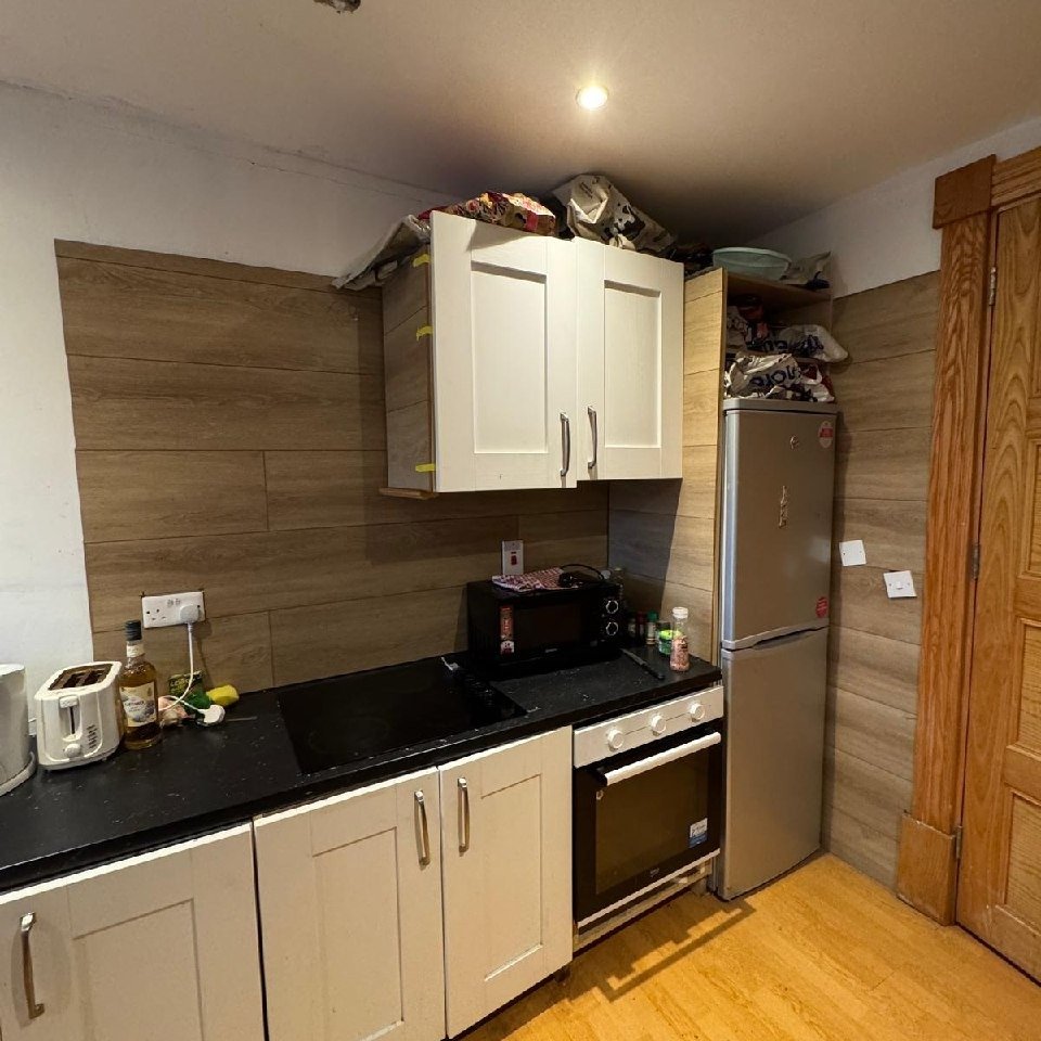 Small kitchen with white cabinets, black countertop, and stainless steel fridge.