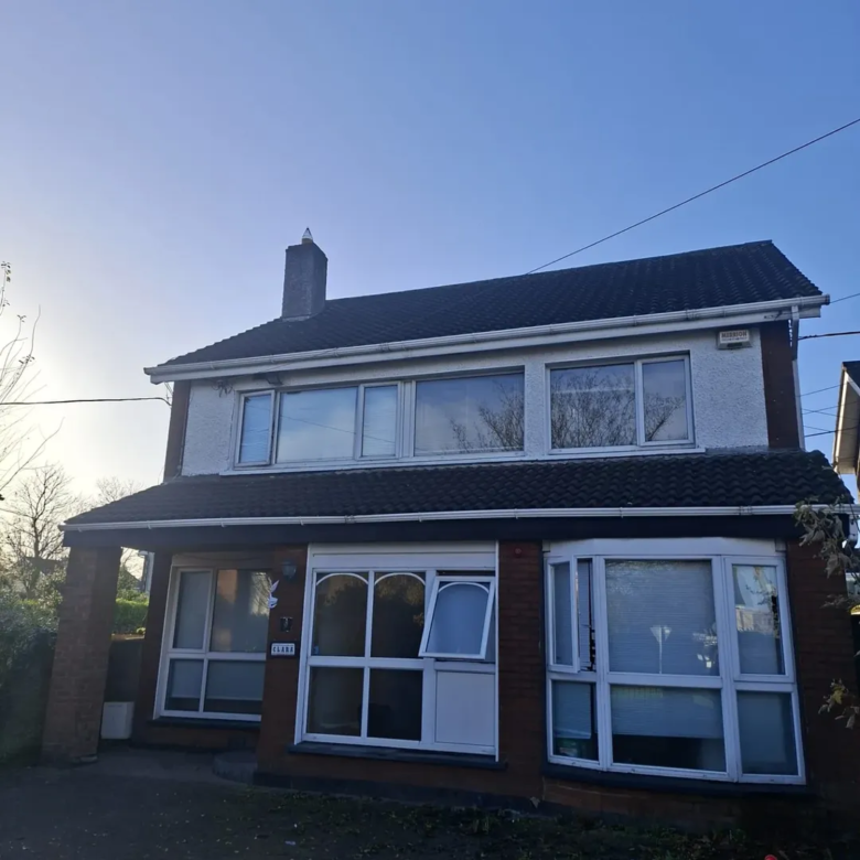 Two-story house with white trim, bay windows, and a dark roof under a clear blue sky.
