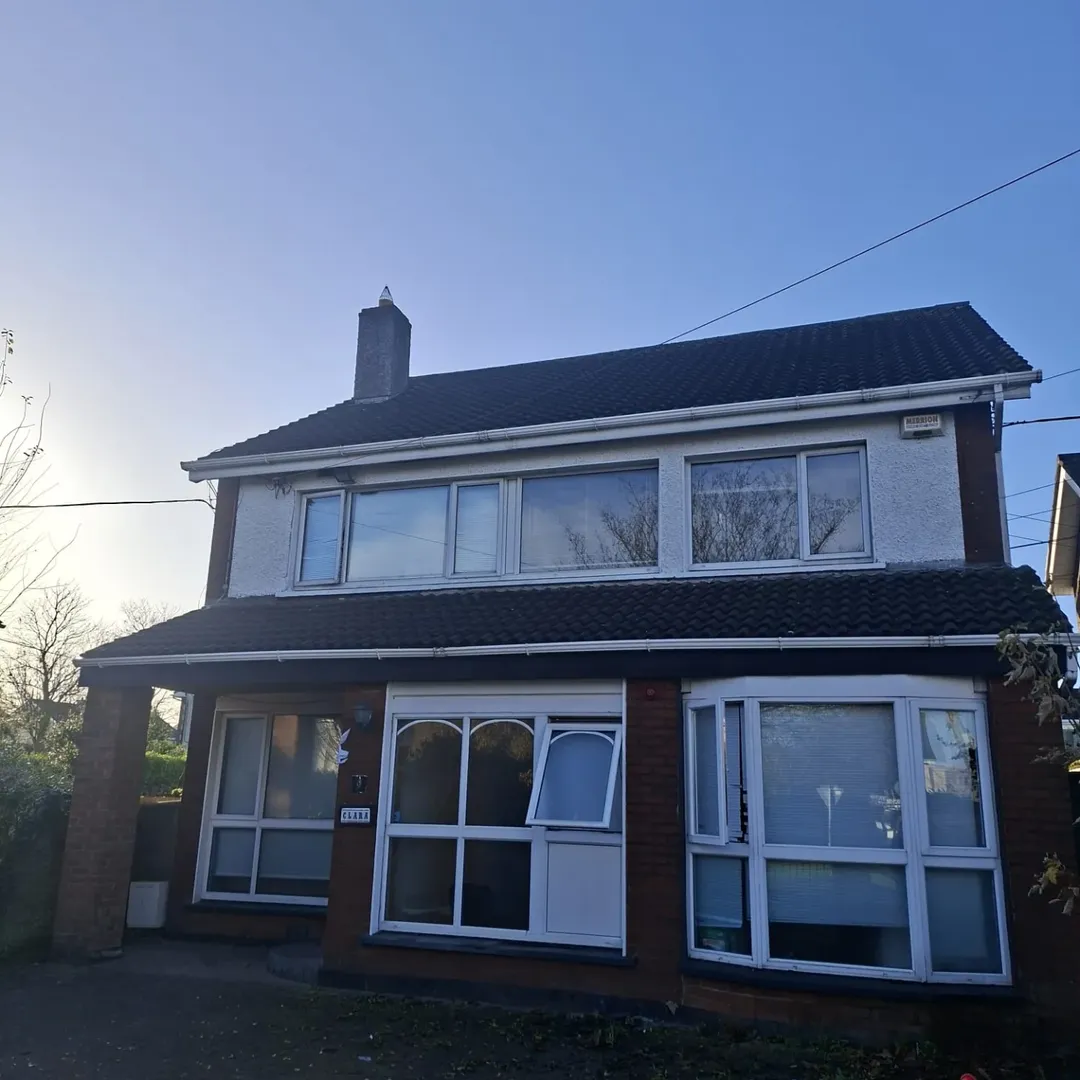 Two-story house with white trim, bay windows, and a dark roof under a clear blue sky.
