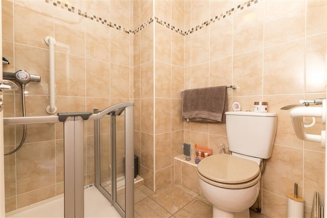 Accessible bathroom with grab bars, beige tiles, and toilet.