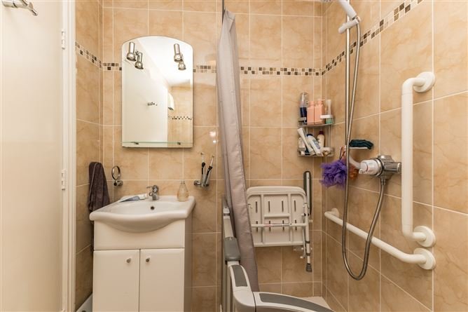 Accessible bathroom with shower seat, grab bars, and beige tile.