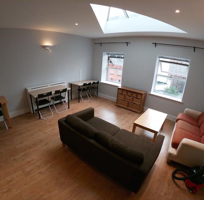 Bright apartment living room with sofas, desks, and natural light from skylight and windows.