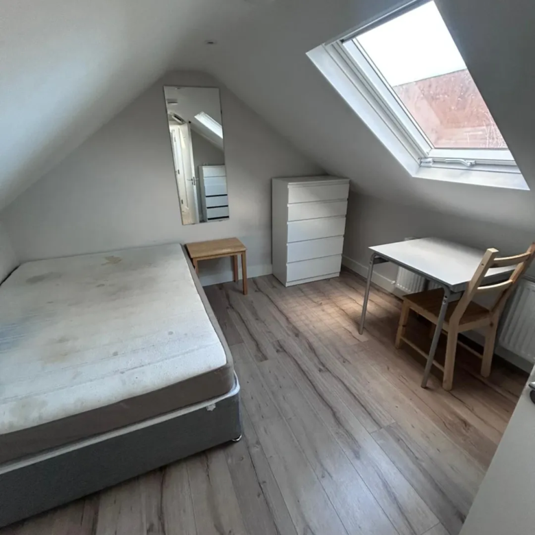 Attic bedroom with bed, desk, dresser, and skylight. Neutral color scheme.