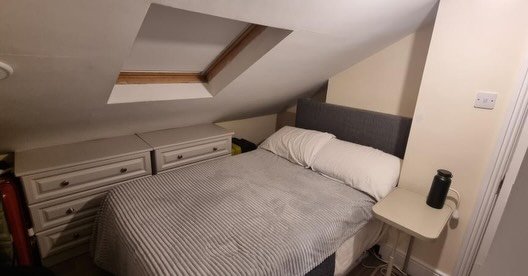 Attic bedroom with double bed, drawers, skylight, and small bedside table.