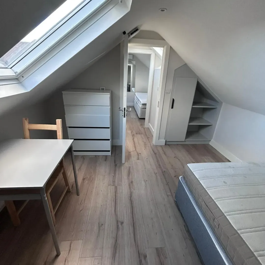 Attic room with skylight, bed, desk, and storage. Bright, minimalist interior design.