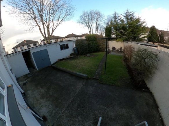 Backyard with garage, lawn, and white walls under a bright sky.