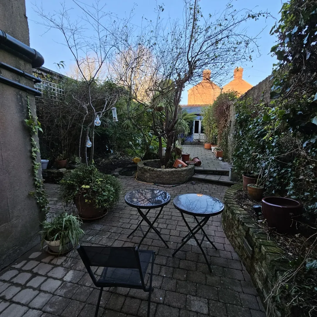 Cozy backyard garden with stone path, potted plants, and small tables.