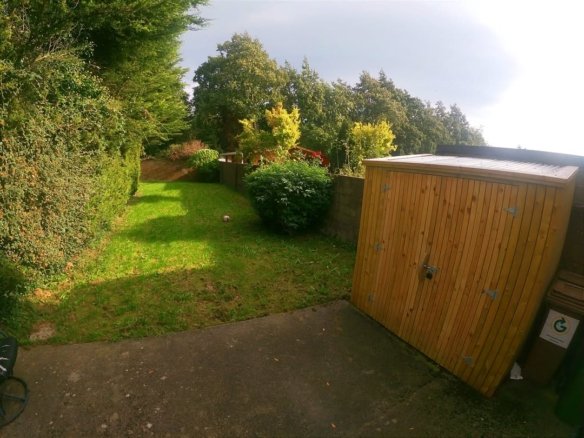 Green backyard with lawn, shed, hedge, trees, and concrete patio on a sunny day.