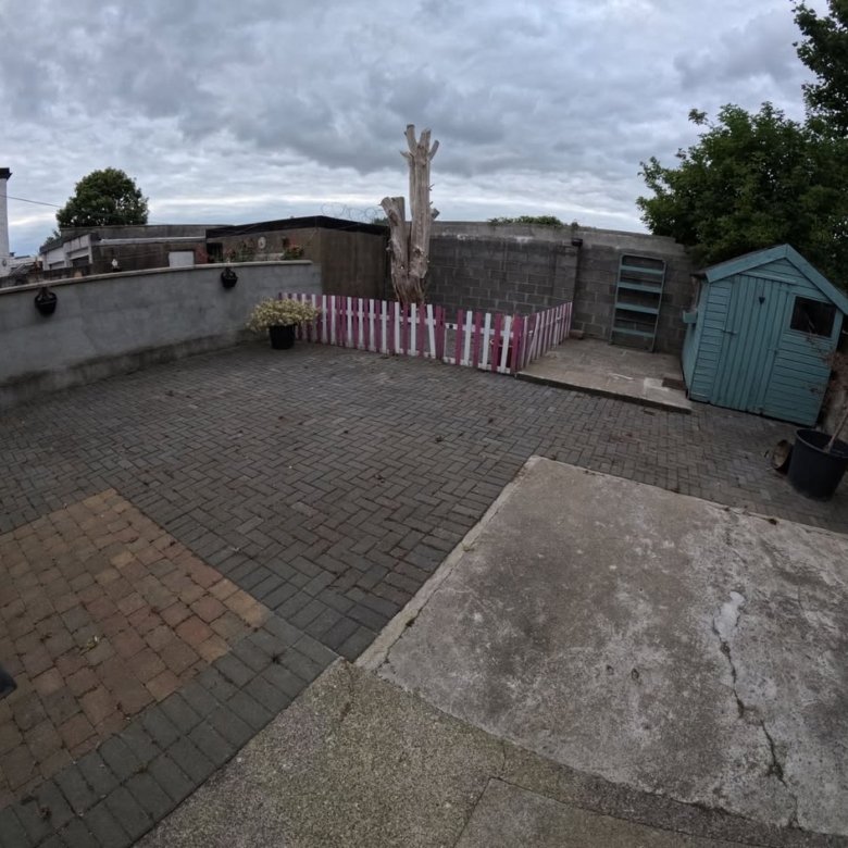 Backyard patio with brick pavers, shed, and pink/white fence under a cloudy sky.