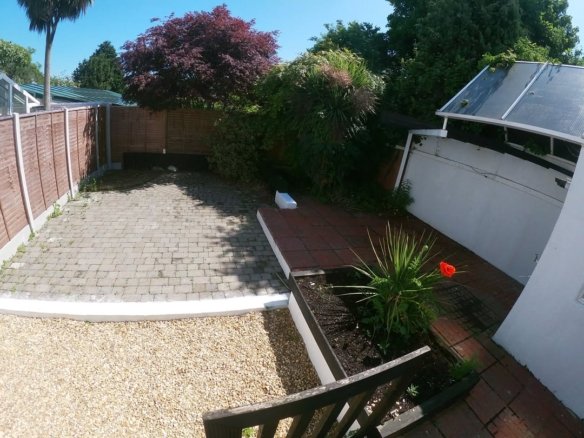 Backyard patio with brick paving, gravel, flowerbed, and wooden fence under a blue sky. Garden landscape design.