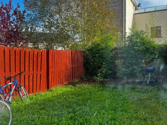 Backyard with red fence, green grass, trees, and bicycles parked beside the fence.