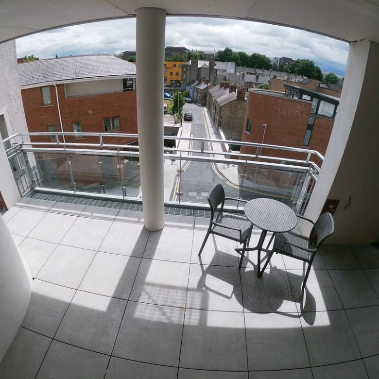 Balcony with table and chairs overlooking street in residential area.